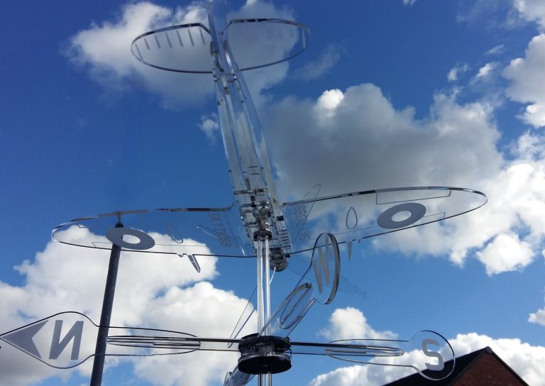 Handmade clear acrylic Spitfire wind spinner against a blue sky